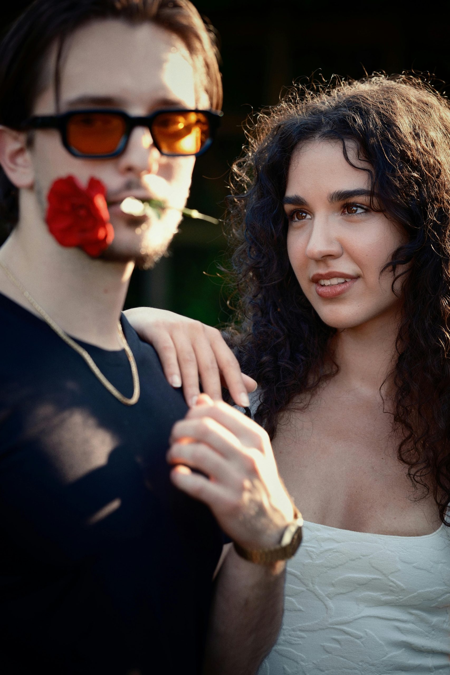 A young couple in a romantic moment outdoors, holding a rose with sunlight casting warm hues.